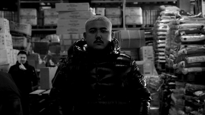 Black-and-white portrait of Big Z in a puffer jacket standing in a warehouse at night