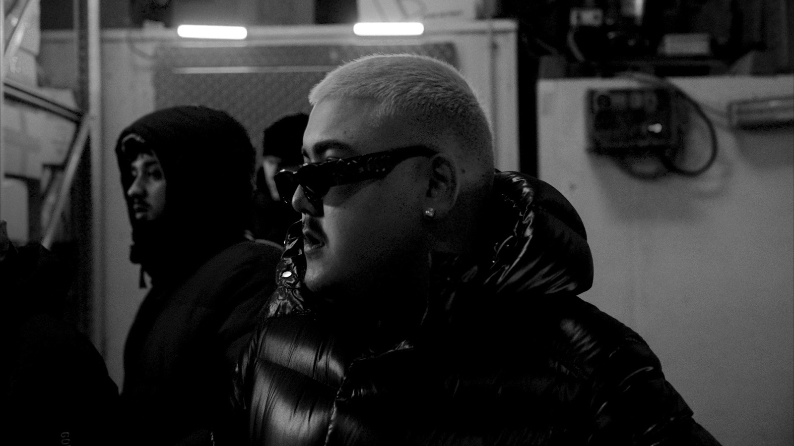 Black-and-white profile of Big Z in dark sunglasses and a puffer jacket on set